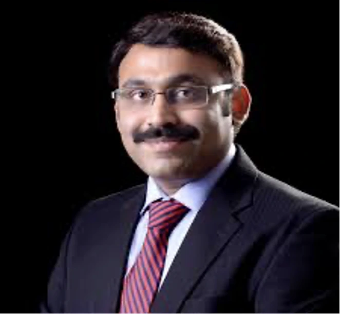 Professional portrait of a man in a dark suit and red striped tie, wearing glasses, against a black background.