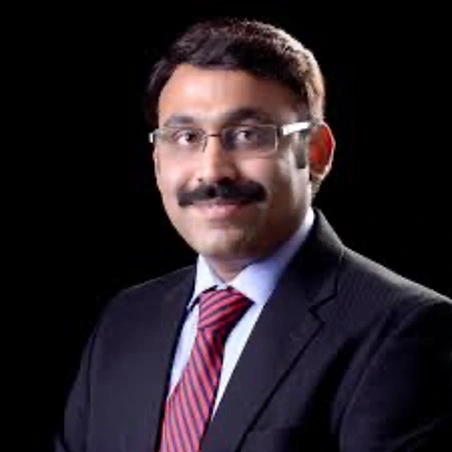 Professional head-and-shoulders portrait of a man in a dark suit and red striped tie against a black background, wearing glasses.