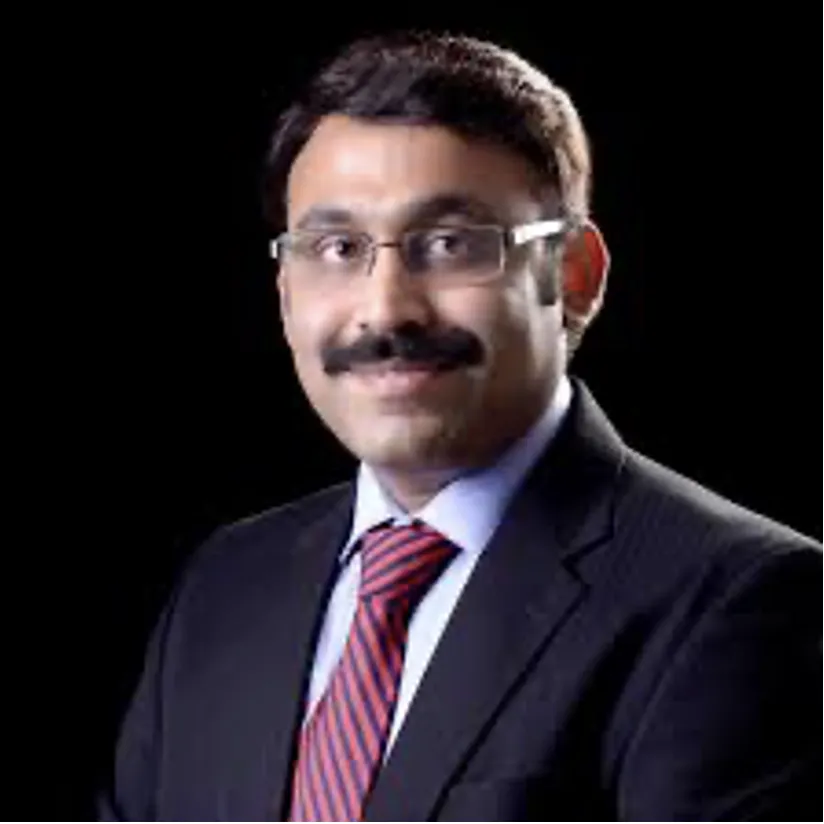 Professional portrait of a man with glasses and a mustache, wearing a dark suit and red striped tie against a black background.